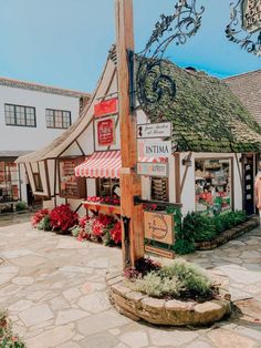 an old fashioned store with flowers in front of it and people walking around the building