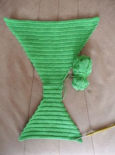 a green knitted tie sitting on top of a bed next to a ball of yarn