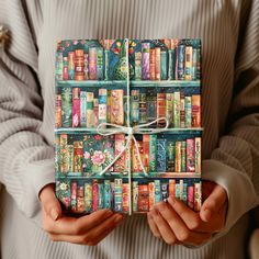 a person holding a book wrapped in paper with bookshelves painted on it's cover