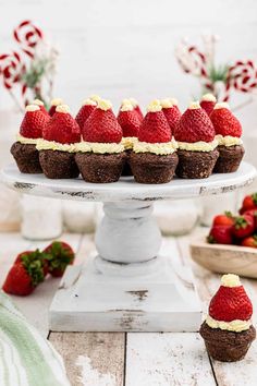 chocolate cups with strawberries and whipped cream on top sitting on a cake plate next to other cupcakes