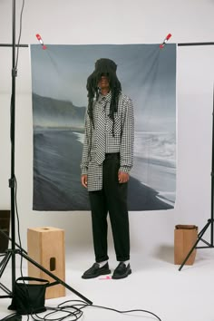 a man with dreadlocks standing in front of a photo on the wall behind him