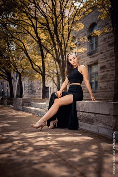 a beautiful woman sitting on top of a stone wall next to trees in the city