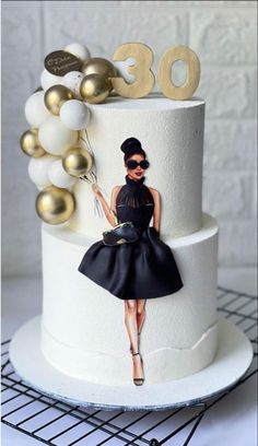 a white cake with a black dress and gold decorations on the top is decorated with an image of a woman in sunglasses