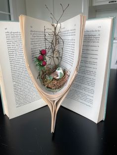 an open book with a bird nest on top of it and flowers in the middle