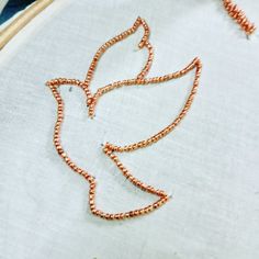 a close up of a piece of embroidery on a hoop with an orange beaded bird