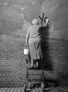 an old woman is leaning against a brick wall and holding a watering can with the words invest in a thermomix on it