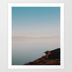 an image of the ocean with mountains in the background and blue sky above it art print