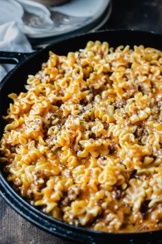 a skillet filled with macaroni and cheese on top of a wooden table