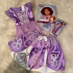 the doll is next to its packaging and it's purple dress with white trim