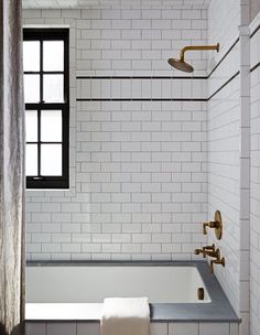 a bath tub sitting under a window next to a shower head and hand held faucet