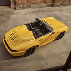 a yellow sports car parked in a parking lot next to a brick wall and door