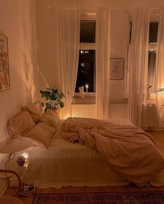 an unmade bed sitting in a bedroom next to two windows with lit candles on them