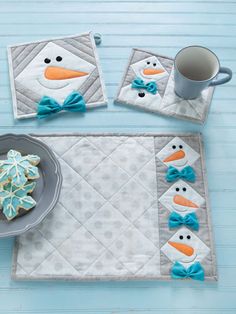 two placemats with snowmen on them next to a cup of coffee and a cookie