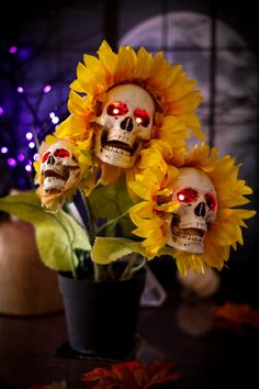 three skulls with red eyes are sitting in a vase filled with yellow sunflowers