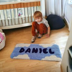 a young boy sitting on the floor in front of a rug that says, daniel