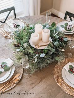 the table is set for christmas dinner with candles, greenery and holly wreaths