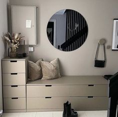 there is a mirror on the wall next to some drawers and a bench with pillows