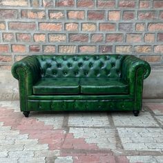 a green leather couch sitting on top of a brick floor next to a stone wall