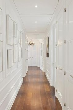 a long hallway with white walls and wooden floors, framed pictures on the wall along one side