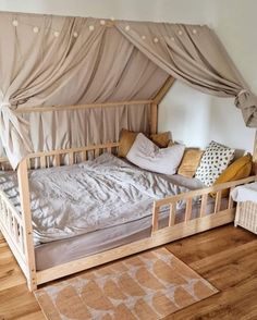 a bed with a canopy over it on top of a hard wood floor next to a white wall