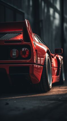 the rear end of a red sports car parked in front of a warehouse building with its lights on