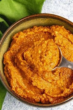 a bowl filled with carrot hummus next to some green leafy leaves and a spoon