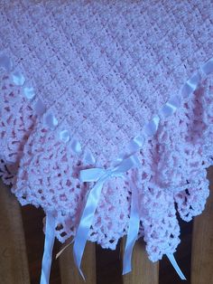 a pink crocheted blanket with white bows on it sitting on top of a wooden chair