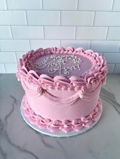 a pink cake sitting on top of a white counter next to a brick wall with the words happy birthday ava written on it