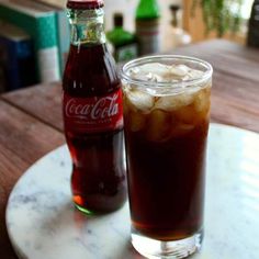 there is a drink on the table with ice and coke in it, next to an empty bottle