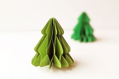 two paper christmas trees sitting next to each other on a white surface with one folded in the shape of an origami tree