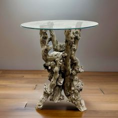 a table made out of driftwood with a glass top on a wooden floor in front of a gray wall