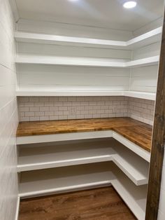 an empty pantry with white shelves and wood flooring on the bottom shelf, next to a brick wall