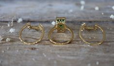 three gold rings sitting on top of a wooden table next to each other with green stones in them