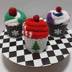 three decorated cupcakes sitting on top of a black and white checkered table