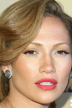 a close up of a woman with earrings on her head and an orange lipstick color