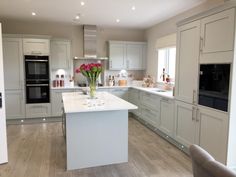 a large kitchen with white cabinets and wood flooring is pictured in this image, there are flowers on the island