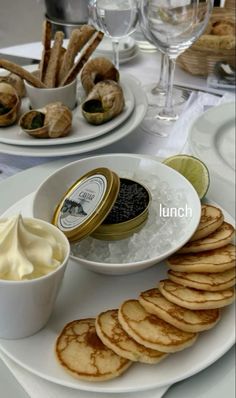 an assortment of food on plates with wine glasses and utensils in the background