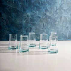 five glasses are lined up on a white counter top in front of a blue background