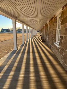 the sun is shining down on a long porch with stone walls and white pillars that are lined with windows