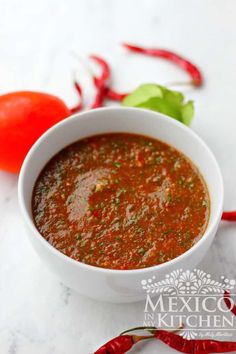 a white bowl filled with red sauce next to some vegetables