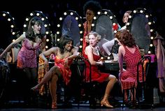 several women in red dresses are sitting at a table with mirrors and lights around them