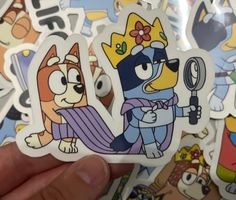 someone holding up some stickers with cartoon characters on them in front of a pile of other stickers