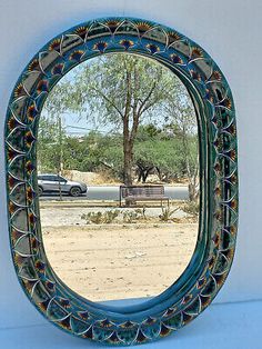 a mirror that is on the side of a wall next to a tree and car