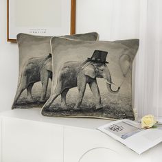 two pillows with an elephant and a man in top hat are on a white dresser