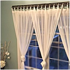 a window with white sheer curtains hanging from it's side