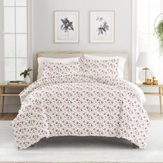 a bed with white sheets and red flowers on it in a room next to two windows