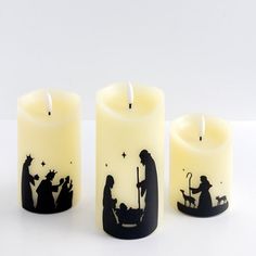 three candles with nativity scene on them sitting next to each other in front of a white background