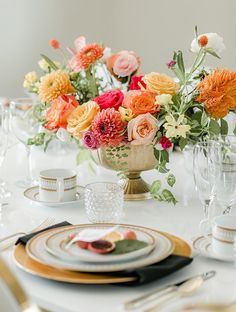 an arrangement of flowers in a vase on top of a table with plates and silverware