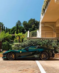 a black and green sports car parked in front of a building with plants on the roof