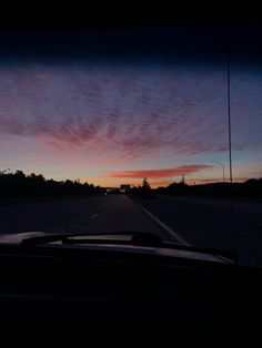 the sun is setting on an empty road with clouds in the sky and cars driving down it